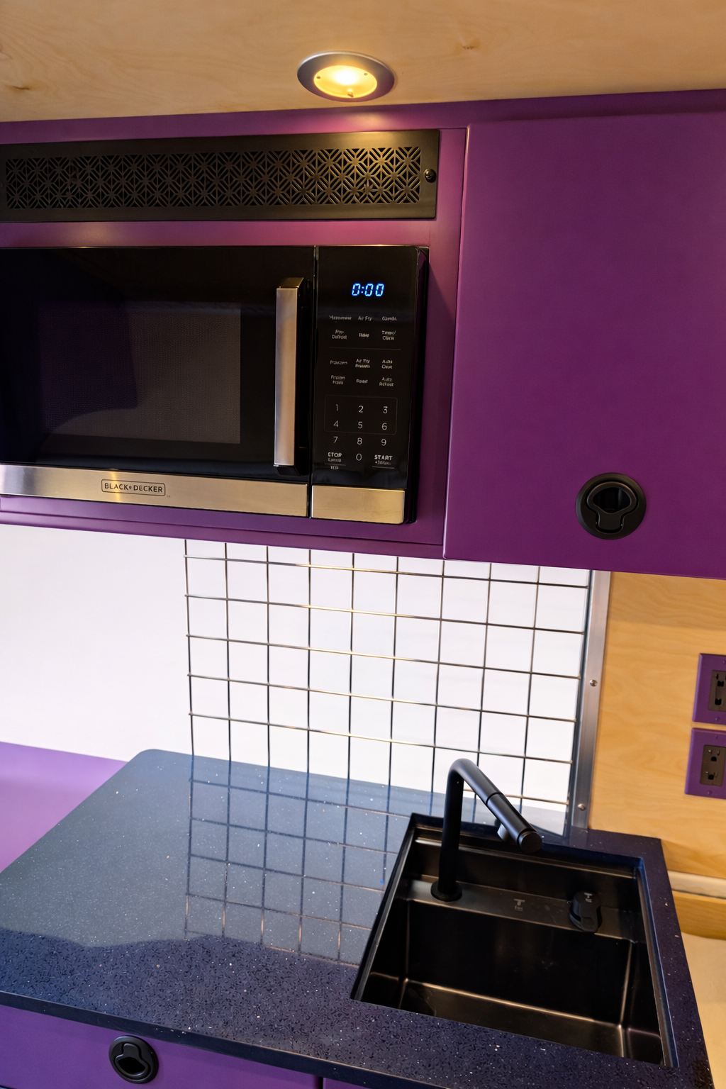 Purple galley cabinetry with black microwave, sink and countertop