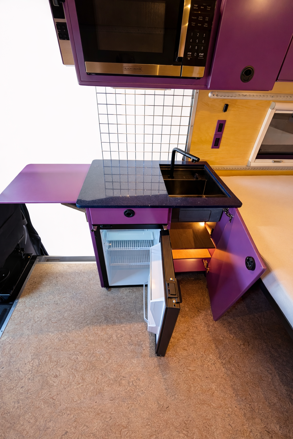 Frida's custom purple galley with black sink, refrigerator, storage and fold-out surface
