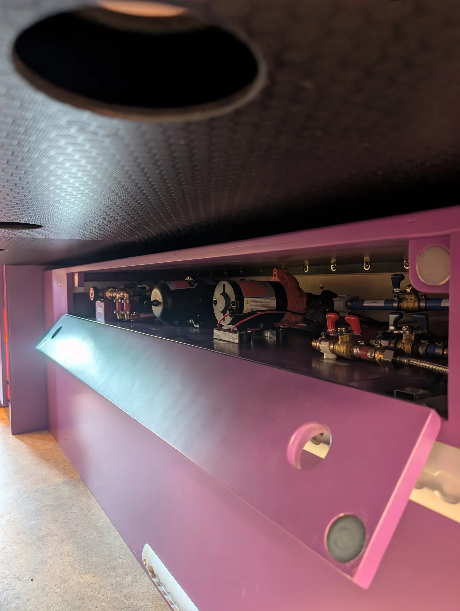 Serviceable water pumps and valves behind a purple drop-down cabinet door